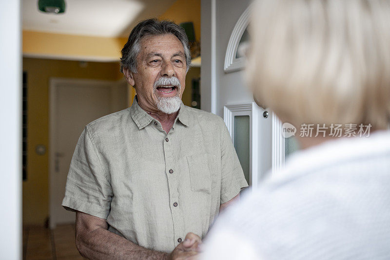 一名老年男子打开前门，迎接一名女性保健工作者进行家庭健康访问