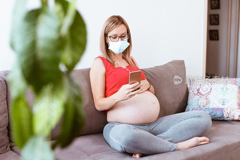 自我隔离的孕妇戴上口罩，用手机预防流行病