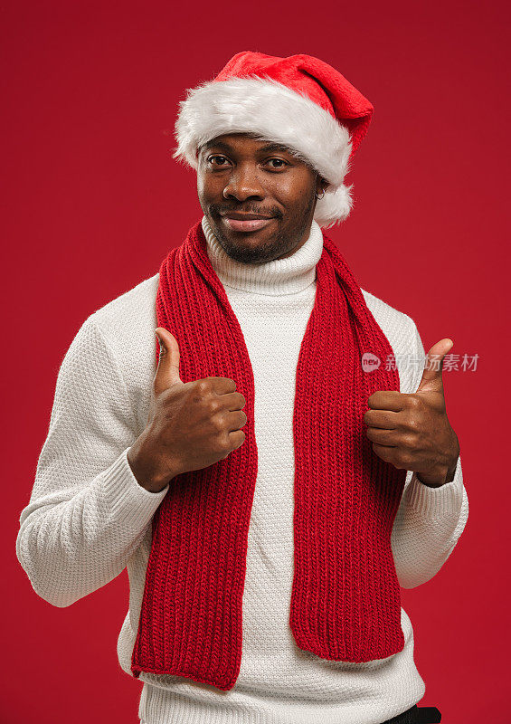 一个穿着羊毛衫、戴着圣诞帽、皮肤黝黑的年轻男子微笑着竖起大拇指