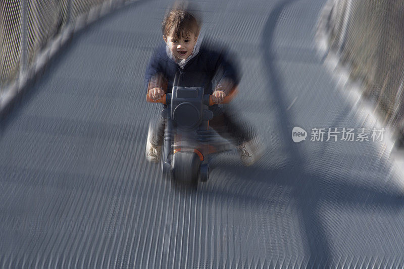 一个小男孩骑着他的小塑料摩托车骑得很快