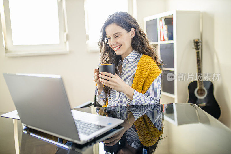 年轻女子在她的家庭办公室边喝咖啡边打视频电话