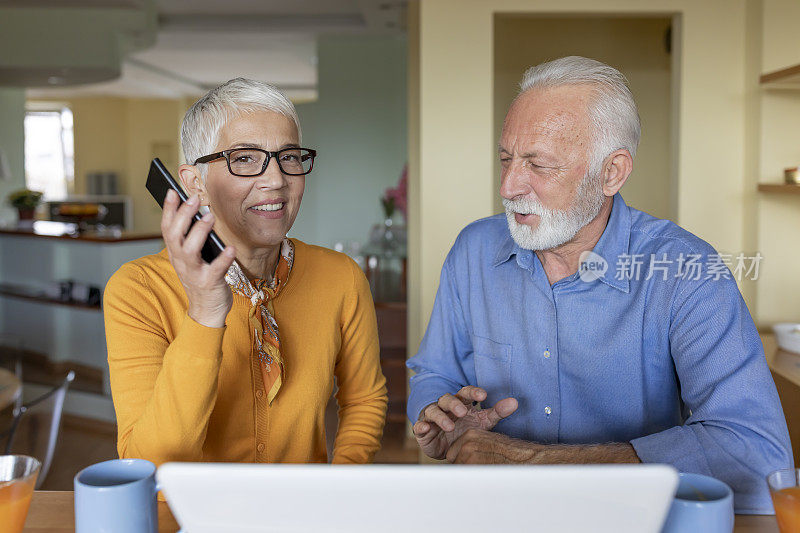 一对快乐的老年夫妇正在享受早上在家里使用笔记本电脑的咖啡。