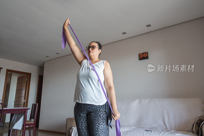 一个成熟的女人在她的客厅里带着阻力带做运动