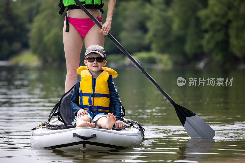 在一个温暖阳光明媚的暑假里，母子站在安静的湖面上划桨