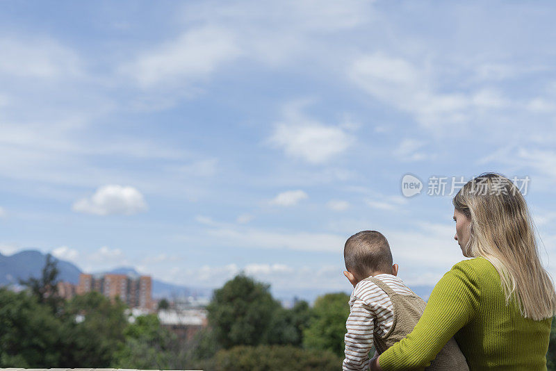 在一个阳光明媚的日子里，母子俩穿着舒适的衣服，从他们房子的阳台上望向别处