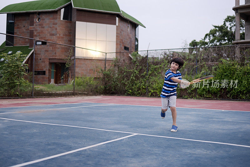 一个混合种族的小男孩在室外网球场打网球