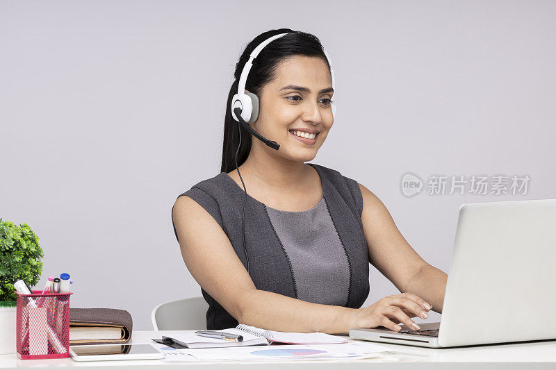 一个有吸引力的年轻商业女性的肖像使用耳机和耳机使用笔记本电脑坐在隔离的白色背景
