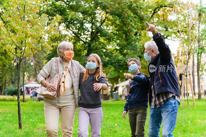 大流行期间，一位老人和他的妻子带着他们的孙辈在城市公园散步。