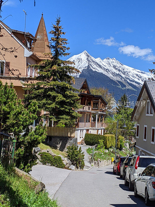 瑞士的阿尔卑斯山耸立在瑞士沃州莱辛村狭窄的街道上，背景是白雪皑皑的阿尔卑斯山