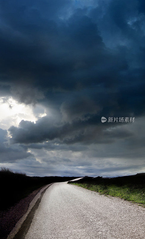 空旷的单车道乡村公路，俯瞰着狂风暴雨的天空