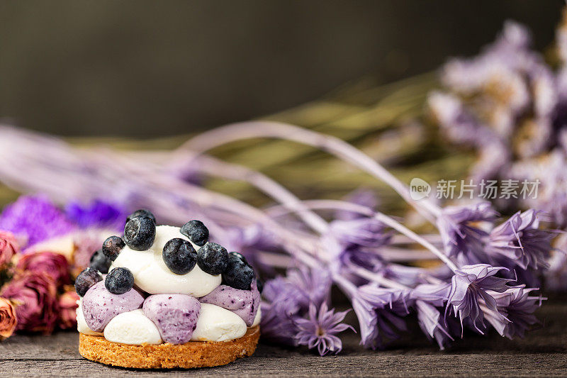 蓝莓格拉汉姆芝士蛋糕，上面有新鲜的浆果，在黑木陈年桌子上，背景是干枯的花朵和树枝。