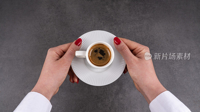 白色杯子里的土耳其咖啡。一只年轻的雌性正拿着盘子里的杯子。