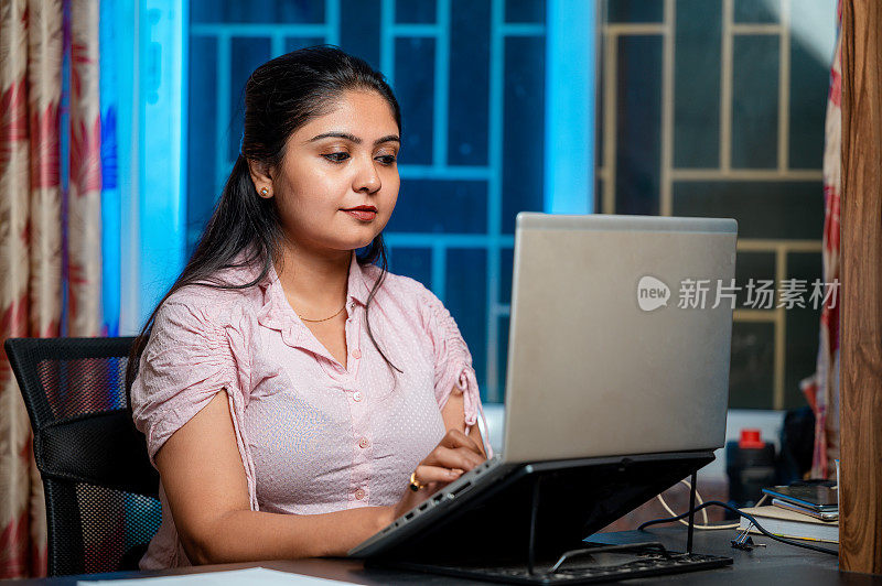 快乐的女人在笔记本电脑上打字，坐在家里办公室的桌子旁工作。