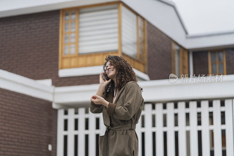 一头卷发的拉丁女子正在屋外用手机打电话