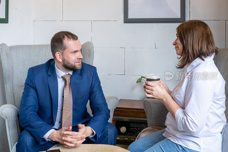 一名身穿白衬衫和牛仔裤的年轻女子端着一杯咖啡，一名中年阿拉伯男子在咖啡馆里聊天