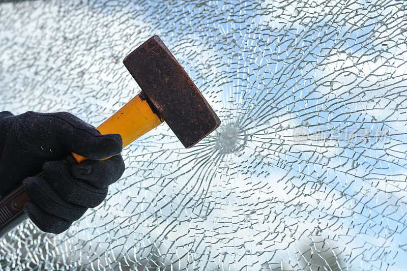 男人的手正从安全玻璃上用重锤敲打窗户，破坏和盗窃的概念，拷贝空间