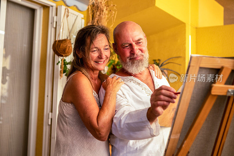 一对自信、快乐的老年夫妇在客厅里画画，享受着他们的闲暇时光和生活