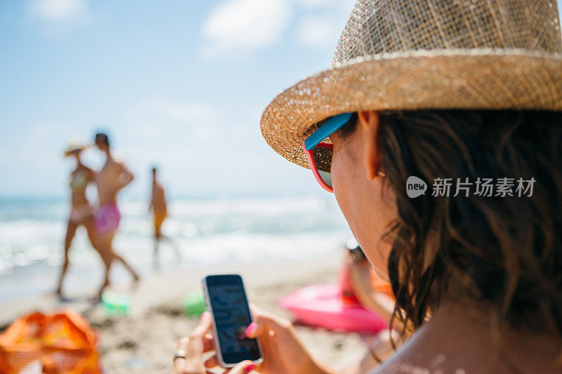 戴着帽子的女人在海滩上用手机