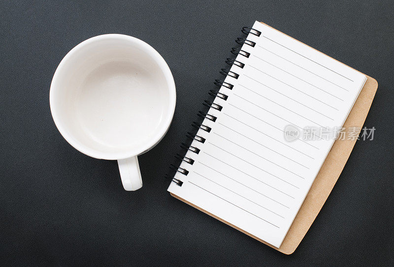 空咖啡杯。在黑色背景上书写的空白笔记本。