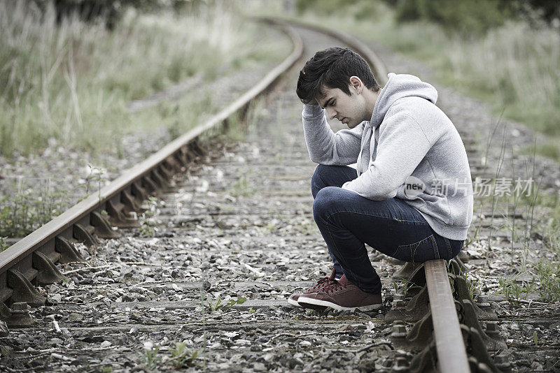 坐在铁路轨道上的沮丧的年轻人