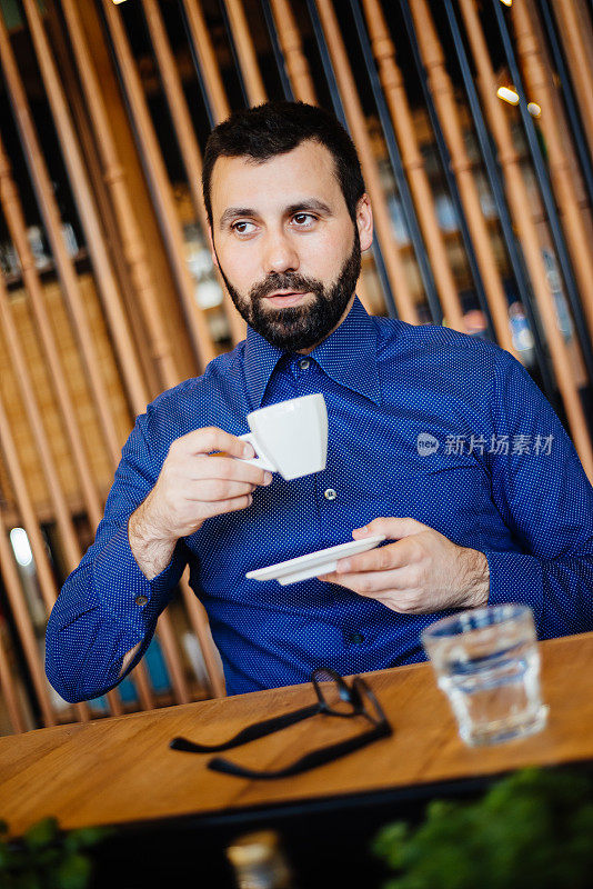 一幅穿着蓝色衬衫喝咖啡的快乐帅哥的肖像