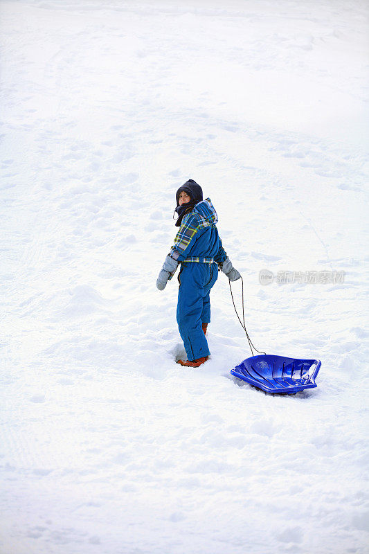 女孩穿着雪衣和塑料雪橇上山