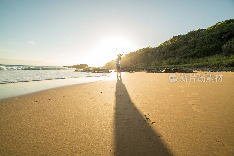 远处的人在日出时在海滩上张开双臂