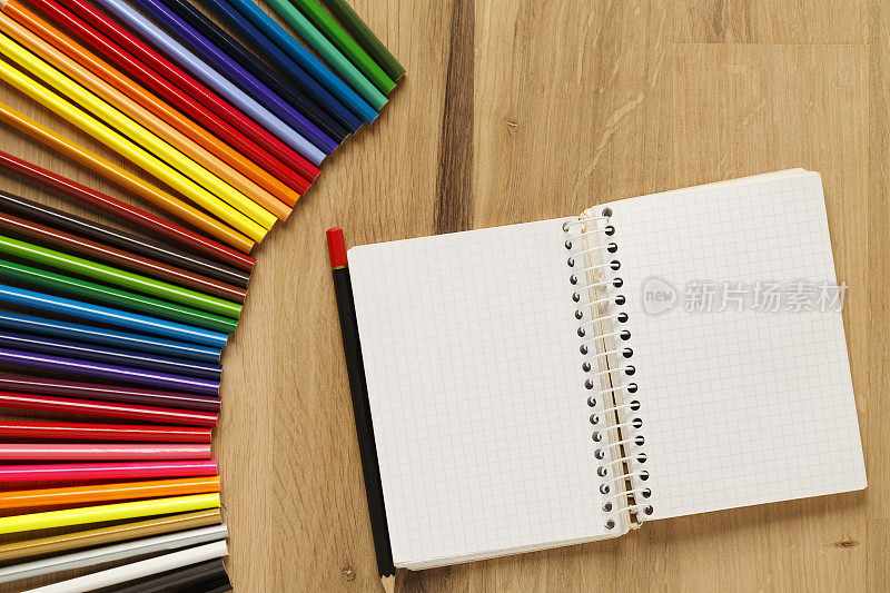 木桌背景上的彩色铅笔空白记事本