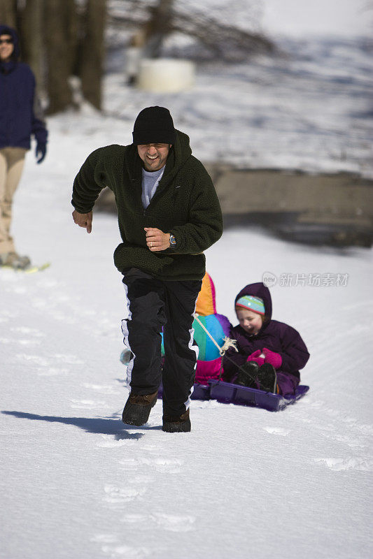 父亲在雪地里用雪橇拉着孩子们