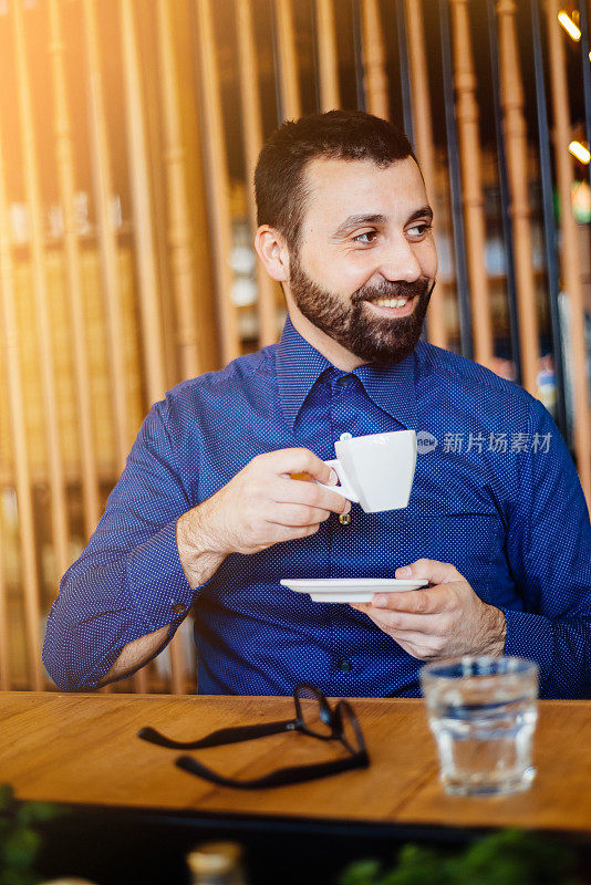 一幅穿着蓝色衬衫喝咖啡的快乐帅哥的肖像