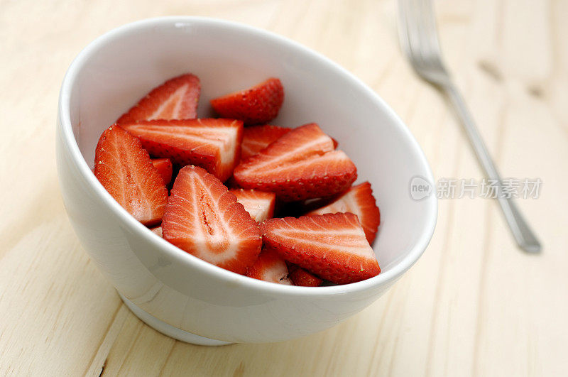 切片熟透的草莓放在碗里，放在橡木桌上