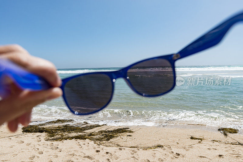 POV手拿太阳镜在海滩上。