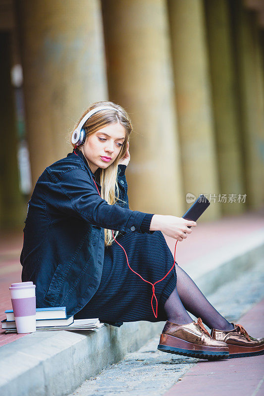 可爱的金发女学生在户外听音乐