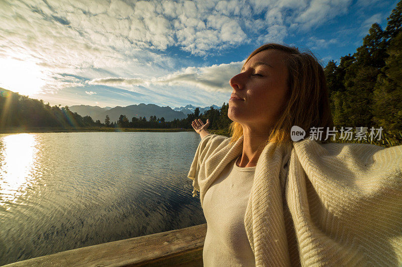 日出时，女人在湖边伸开双臂