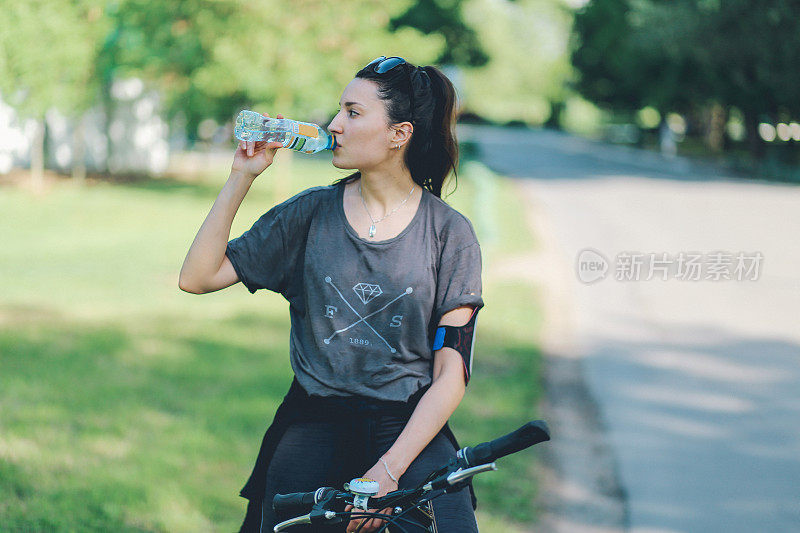 年轻女子在自行车上喝水