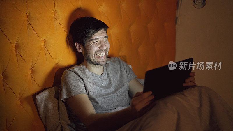 睡觉前躺在床上用平板电脑浏览社交媒体的年轻笑男