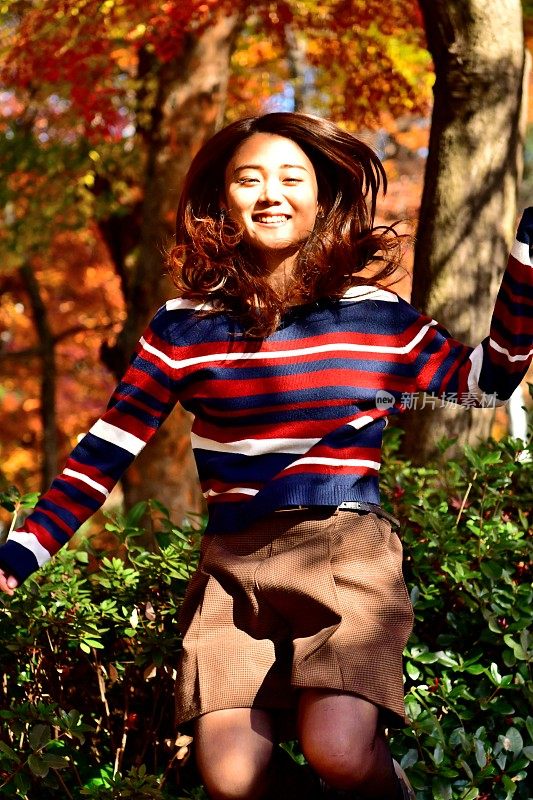 一名年轻的日本女子在东京的秋色公园里跳跃