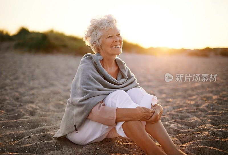 愉快的老妇人坐在海滩上