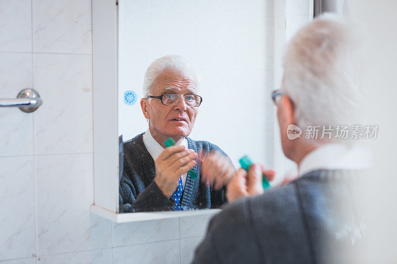 老年人在家里。老男人看着浴室的镜子，穿衣服，整理头发