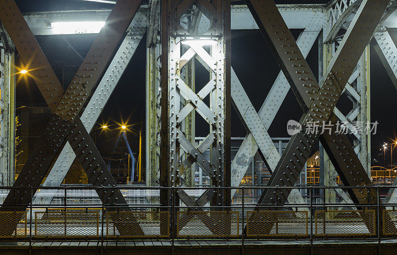沥青路面下的钢结构城市桥梁。夜晚的城市场景和隧道里的车灯痕迹。健美的