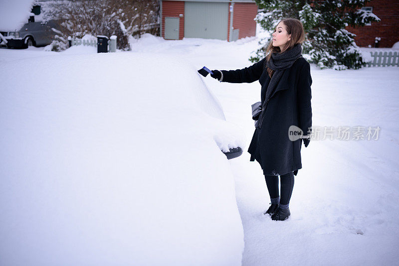 冬天即将来临。女人在冰冷的天气里，车被雪覆盖着。