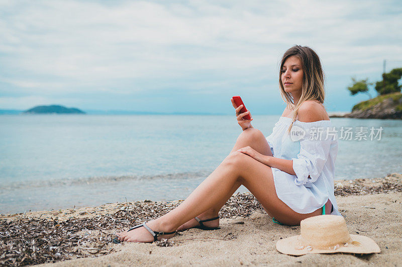 年轻女子戴着太阳帽坐在海滩上看海