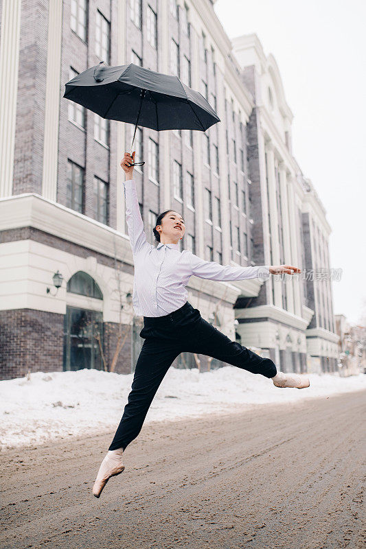 芭蕾舞女演员手里拿着伞在城市街道上跳高。