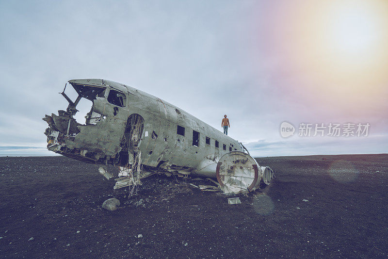 一个年轻人站在飞机坠毁的黑沙滩上，环顾四周，思索着周围的一切