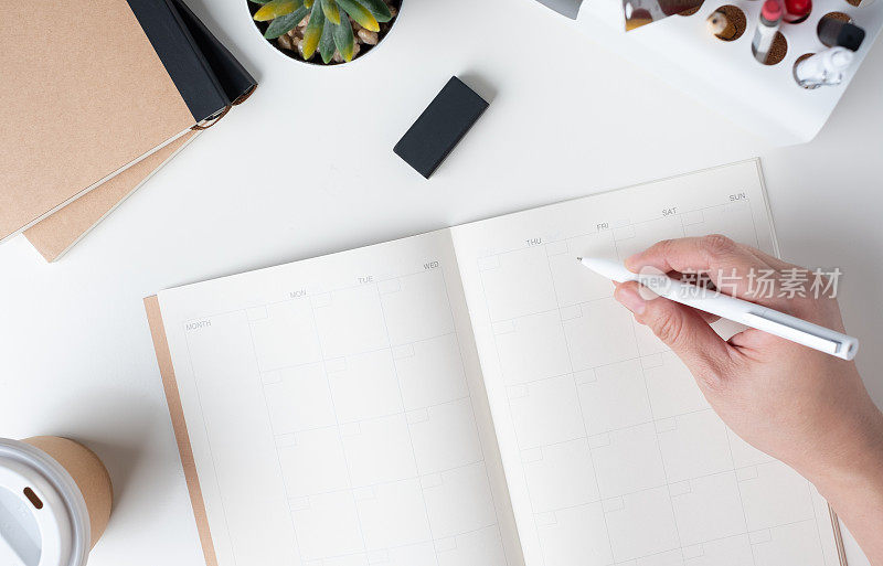 俯视图手写的开放式日历计划的商务决议与现代办公文具和带走咖啡杯在白色的办公桌在办公室。模拟空间的组织者桌子笔记本。
