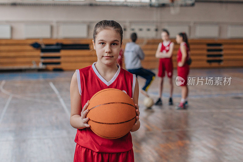 可爱的女孩篮球运动员拿着篮球在球场上