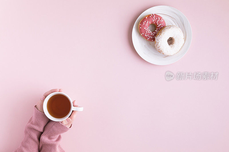 早上的咖啡杯和甜甜甜圈放在粉色柔和的桌子上，俯视图。平铺一层舒适的早餐