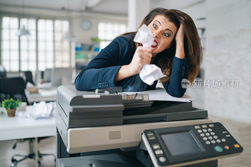 一位恼怒的女商人站在办公室的打印机前