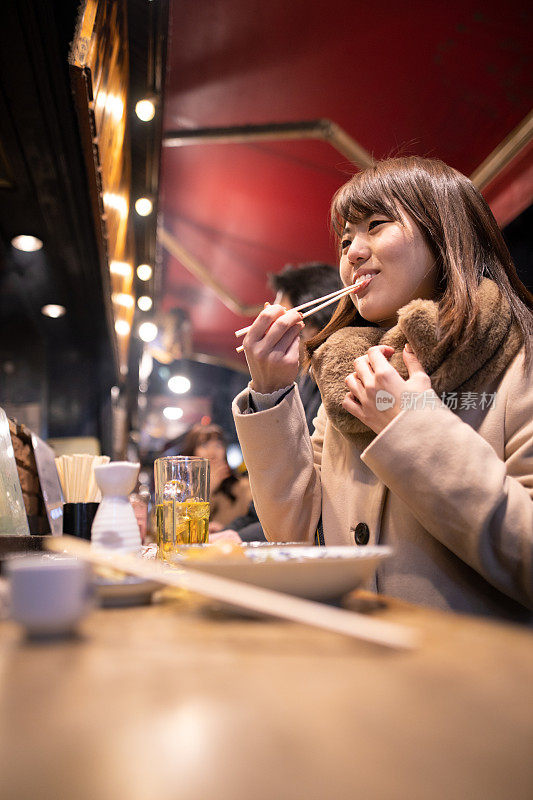 年轻女子在户外站居酒屋酒吧吃日本当地食物