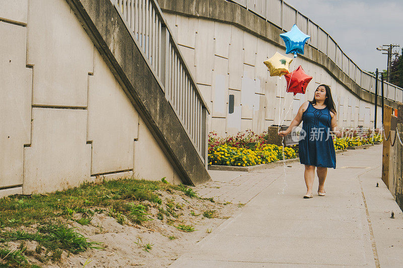 可爱的中国女人拿着三个气球沿着水泥墙走